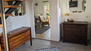 Ein Zimmer mit einer Holztreppe, einem Schreibtisch mit einer Artikelliste, einem Schmuckkästchen und einer gemütlichen Sitzecke mit Sofa und Sesseln.