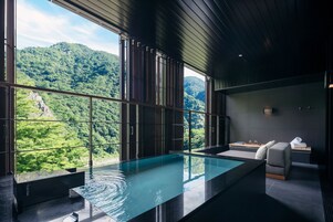 A modern bathroom with a glass-enclosed infinity pool, a seating area, and a view of a lush green landscape.