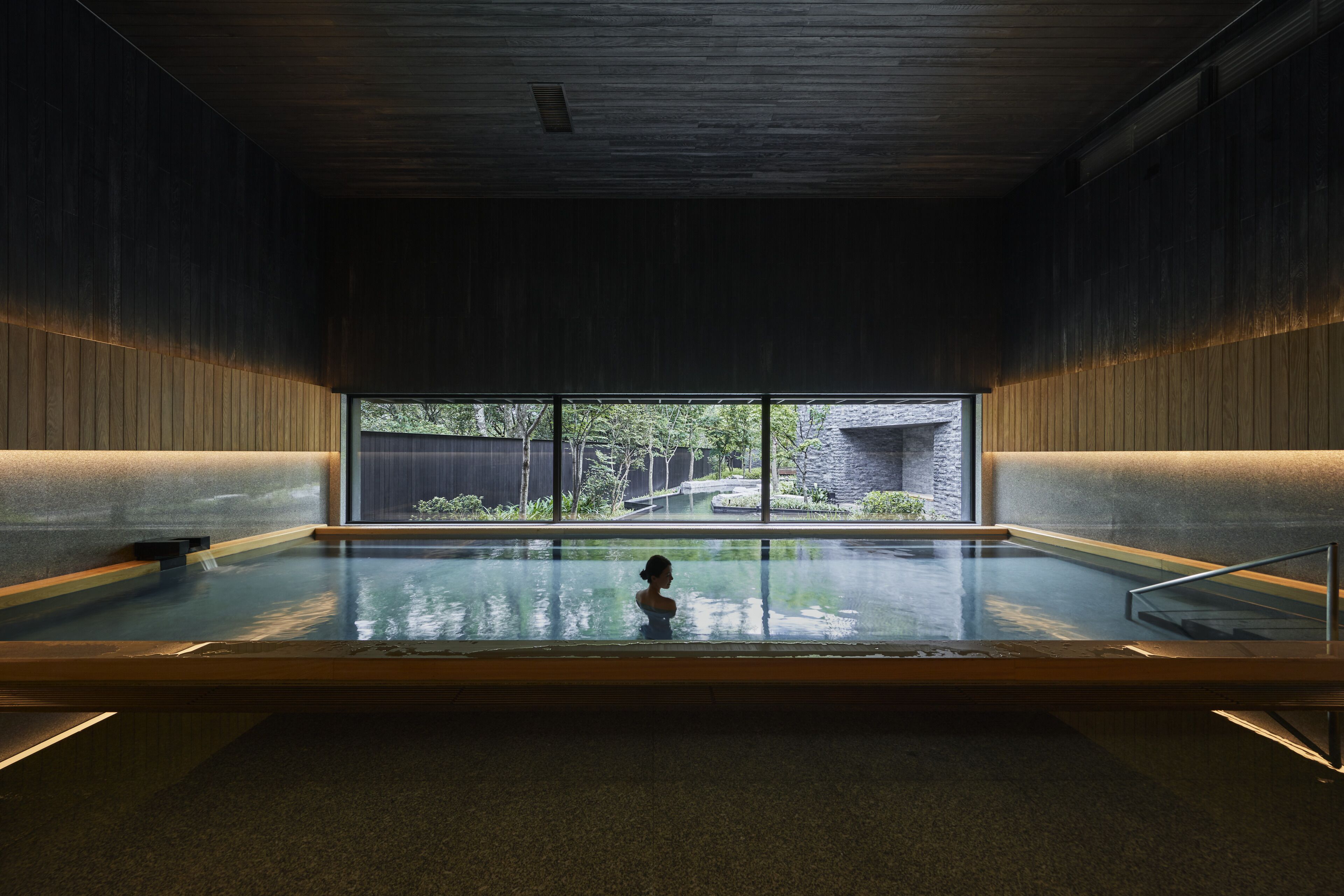 Una amplia piscina interior con vistas a un jardín y una construcción de piedra al exterior.