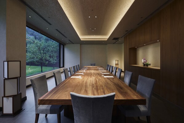 A conference room with a long wooden table, grey upholstered chairs, and a view of trees through large windows. - HOSHINOYA Guguan (Taichung)