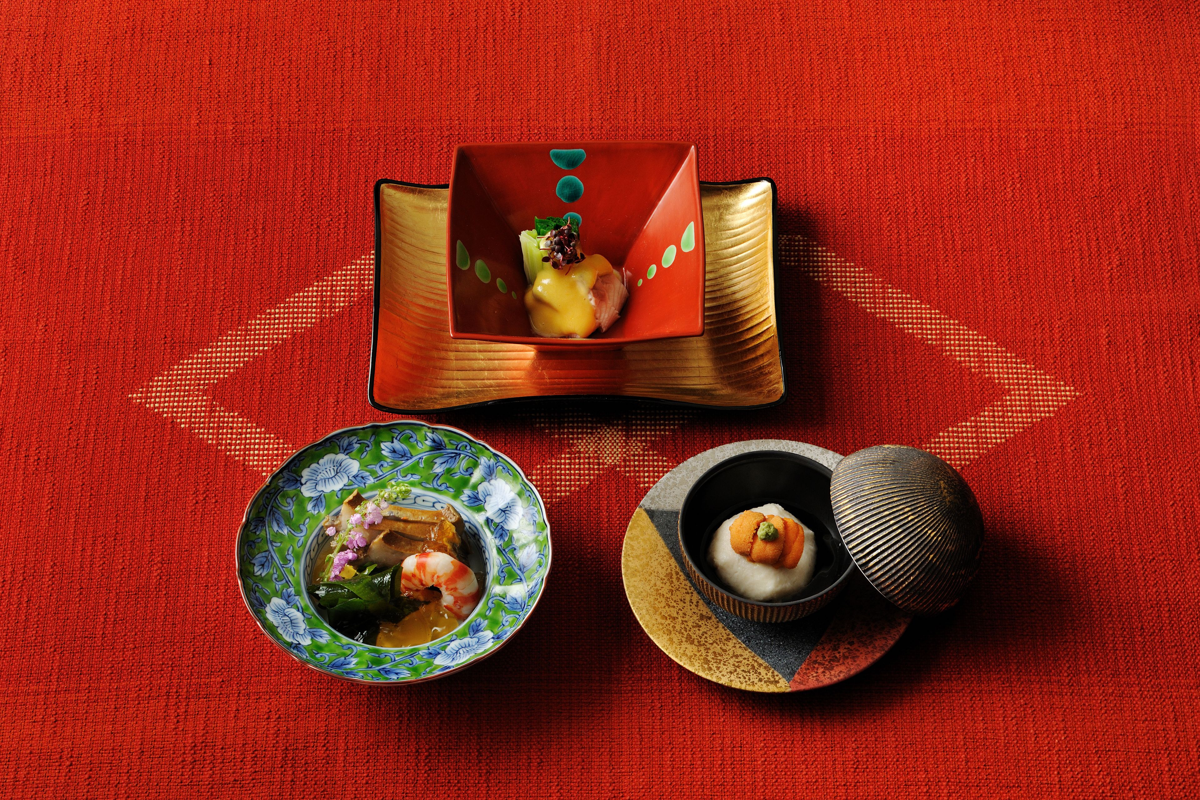A table with three dishes: a bowl of soup with vegetables, a plate with a fish dish, and a bowl with a dessert.