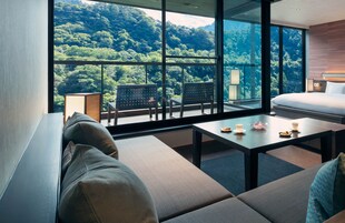 A modern hotel room with a large balcony, a sofa, a table with tea cups, and a bed.