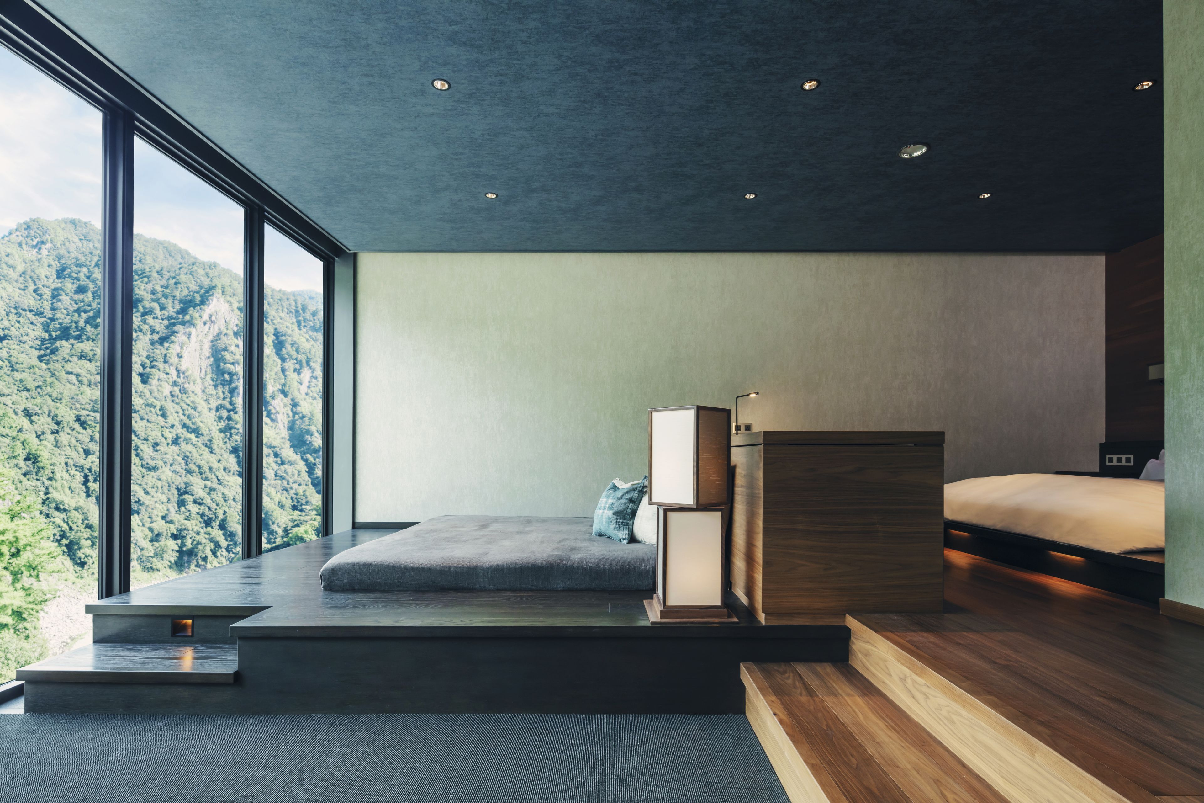 A modern bedroom with a large window, a bed, a nightstand, and a built-in bench.