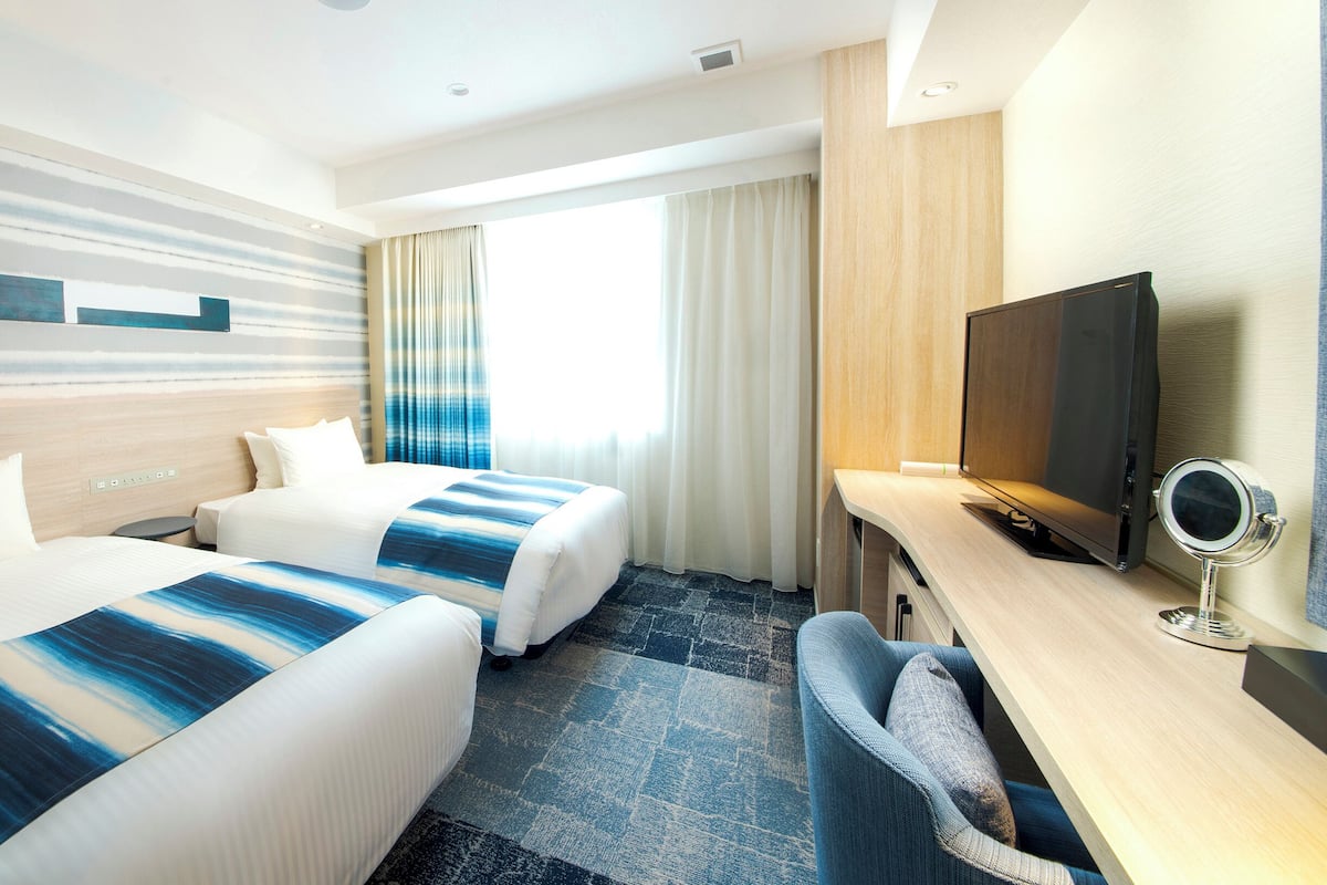 A hotel room with two beds, a desk with a TV, and a mirror.