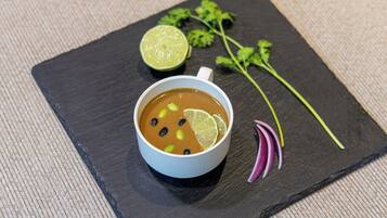 A bowl of soup with black beans and lime slices on a black slate plate, accompanied by a half lime and a bunch of cilantro.