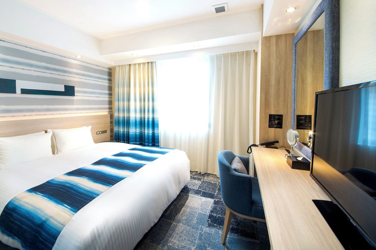 A hotel room with a large bed, a desk with a TV, and a mirror.