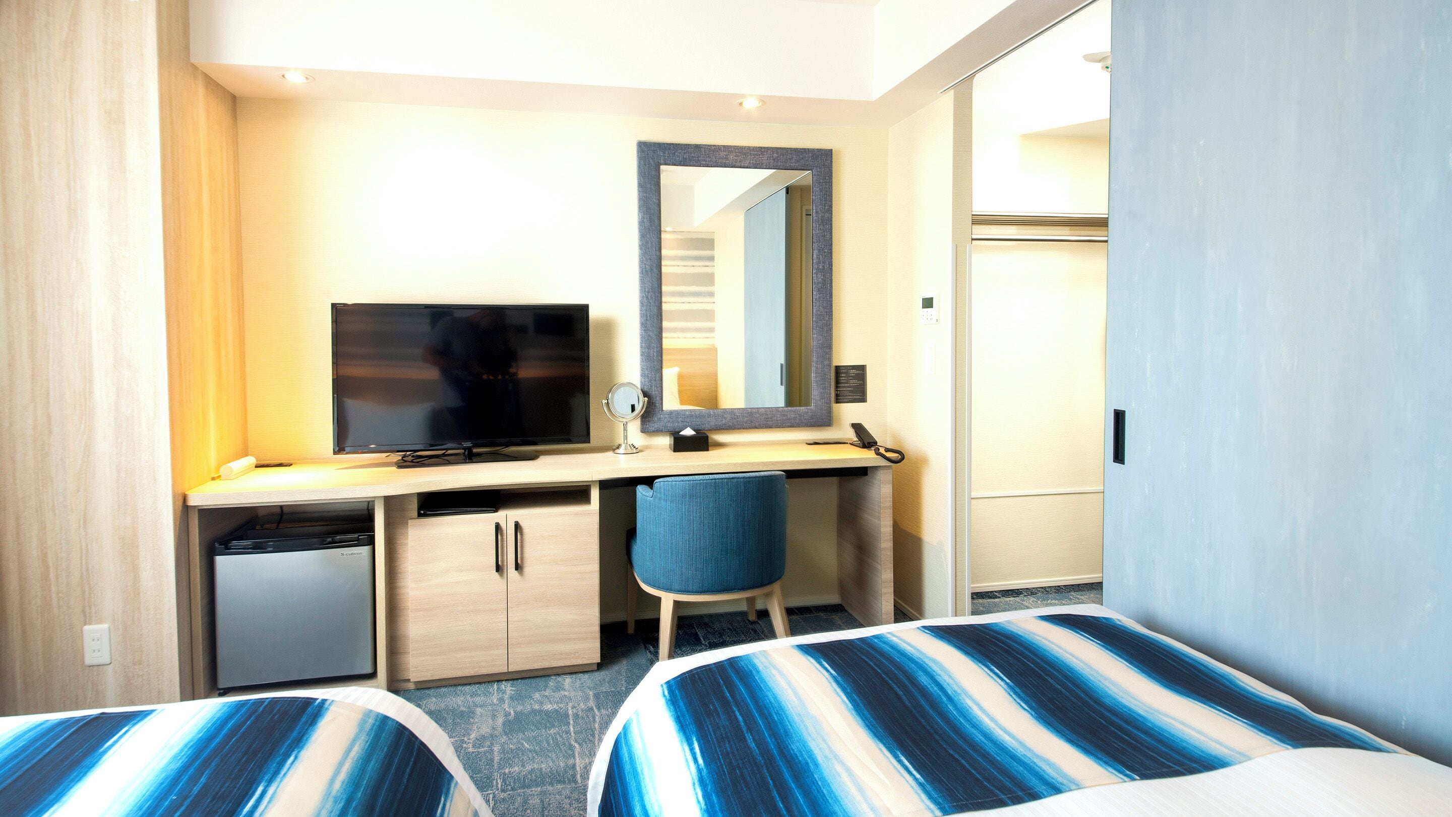 A hotel room with a bed, a desk with a TV, a chair, and a mirror.