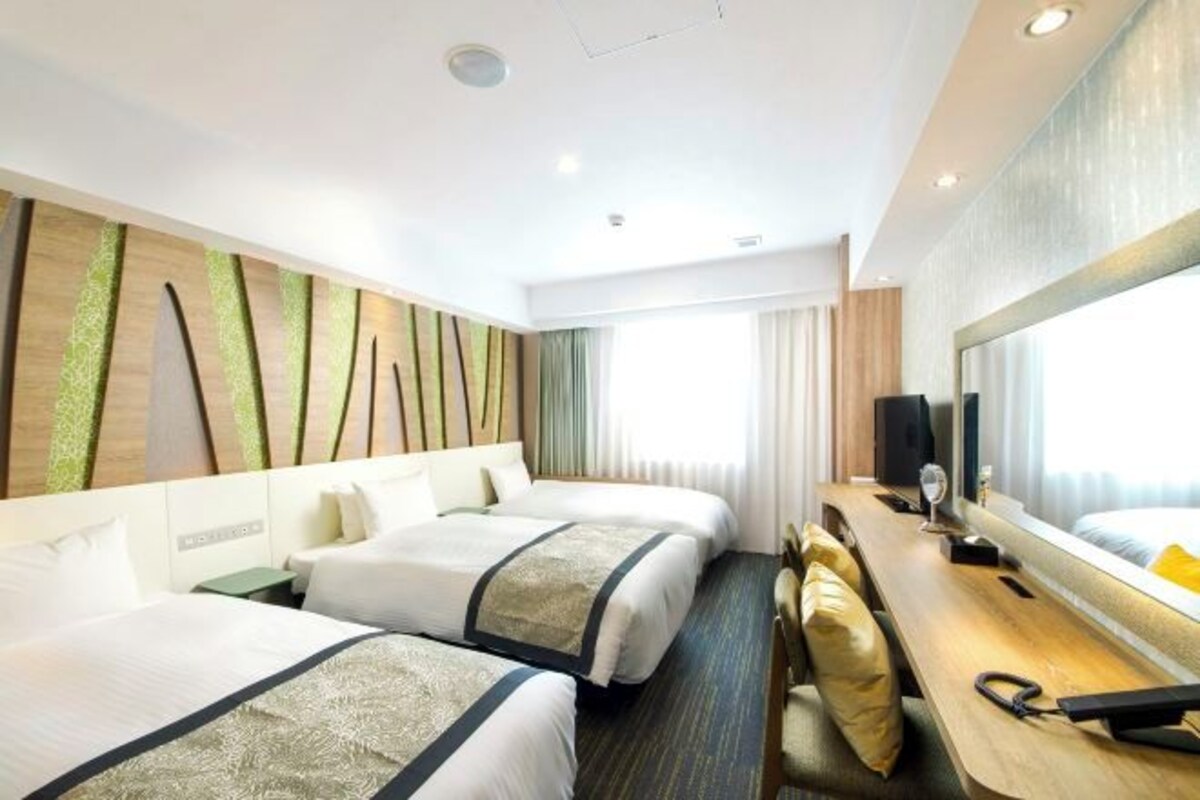A hotel room with two beds, a desk, a chair, a large mirror, and a television.
