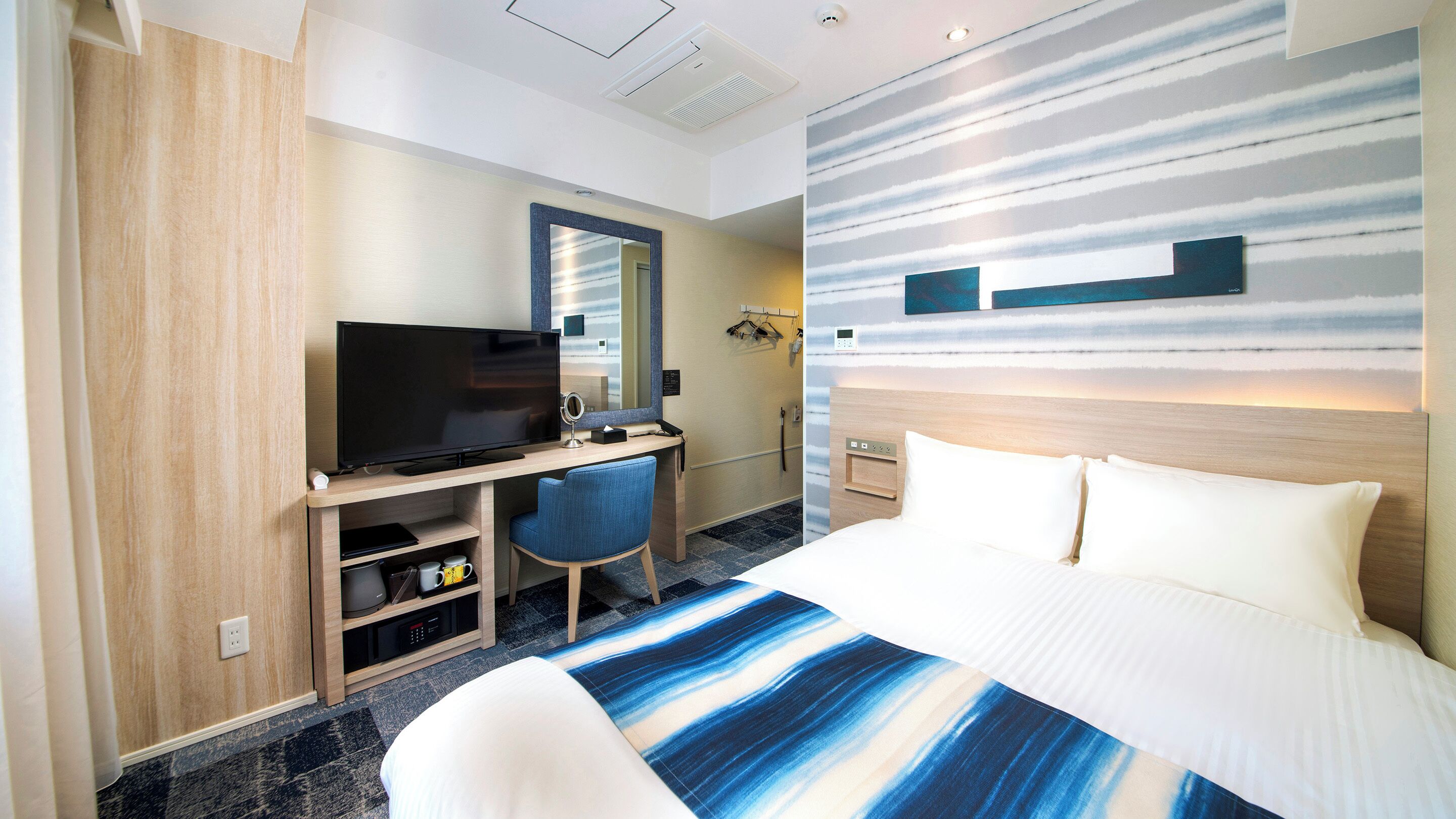 Une chambre d’hôtel moderne avec un grand lit, un bureau avec une télévision, un miroir et un espace douche.
