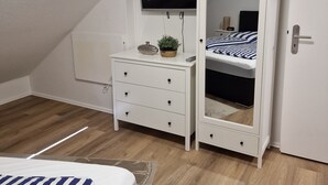 A bedroom with a bunk bed, a dresser with drawers, a television mounted on the wall, and a door. - Holiday apartment directly on the beach of the North Sea and still central in Bensersiel (Bensersiel)