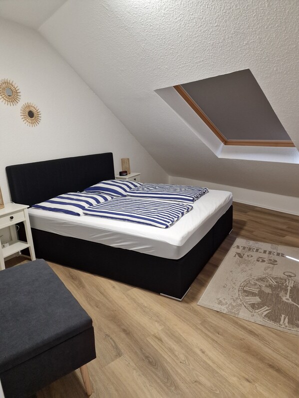 A bedroom with a bed, a nightstand, a desk, and a skylight.