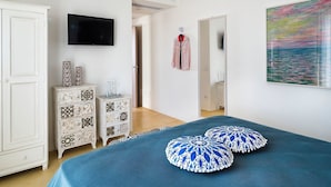 A bedroom with a bed, a wardrobe, a TV, a painting, and a door leading to another room. - Villa Ulivo for 8 People in Sicily, Pool, Sea View, Garden, Wifi and A/C (Reitani)