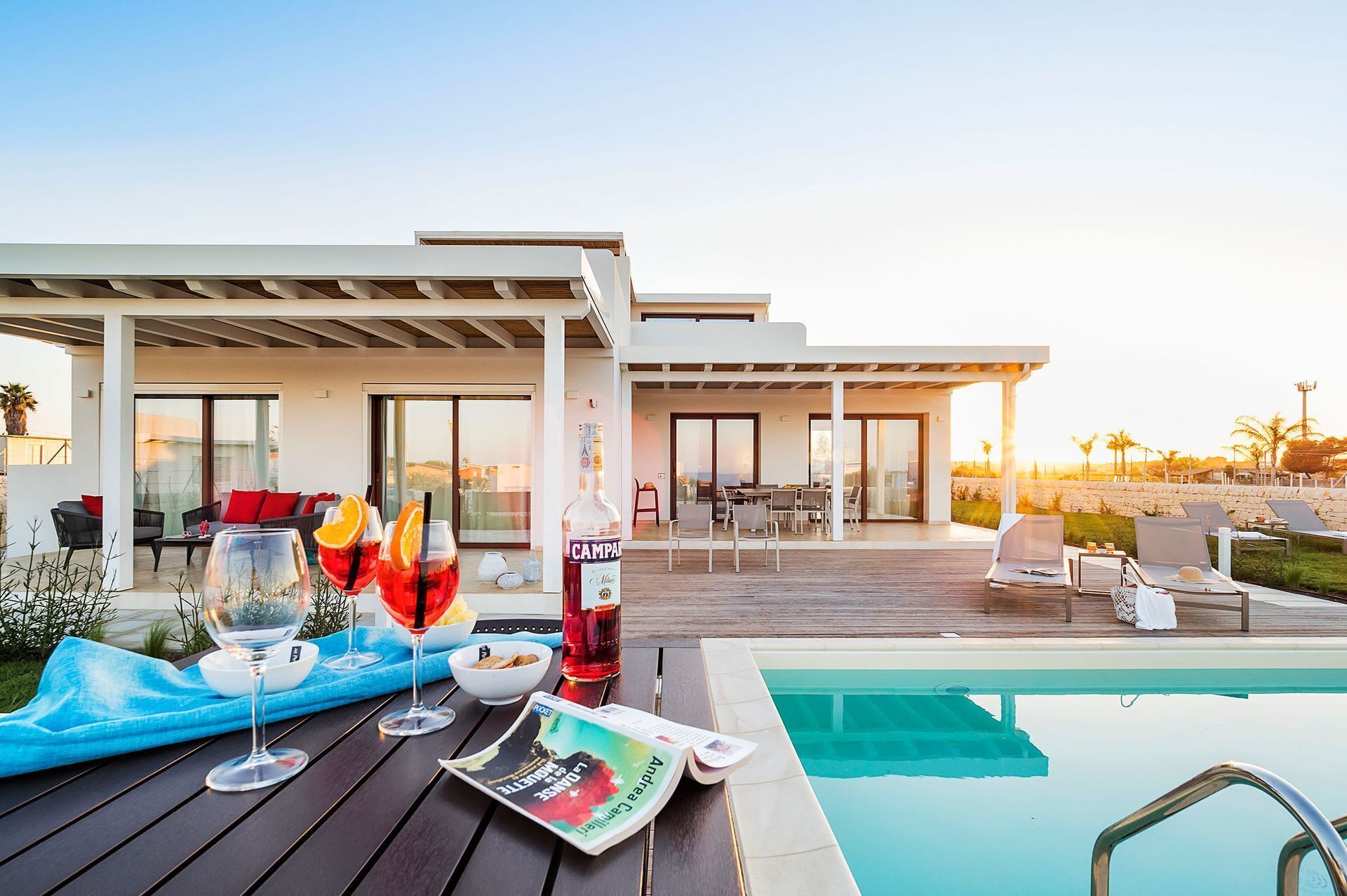 Ein moderner Poolbereich im Freien mit Holzterrasse, Liegestühlen und einer patioartigen Veranda mit Essmöbeln.