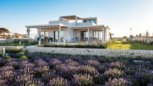 A modern two-story house with a patio area, a swimming pool, and a garden with purple flowers. - Villa Ulivo for 8 People in Sicily, Pool, Sea View, Garden, Wifi and A/C (Reitani)