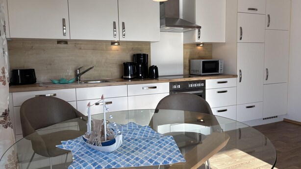 Una cucina moderna con mobili bianchi, elettrodomestici in acciaio inossidabile e un tavolo da pranzo in vetro con sedie.
