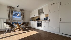 Una cucina moderna con mobili bianchi, un forno a microonde, un forno e un'area pranzo con un tavolo e sedie in legno.