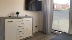 A modern room with a grey cabinet, a flat-screen TV mounted on the wall, and a sliding glass door leading to an outdoor area. - The "Seepferdchen" in Haus Meeresglück, close to the beach and central! (Dahme)
