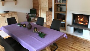 A cozy room with a wooden floor, a purple table with candles, chairs, a bookshelf, and a fireplace.