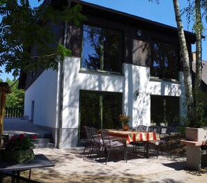 A modern two-story house with a patio area featuring a table and chairs, surrounded by trees. - NEW - Cottage on the lake only 750m forest path to Libbesickesee (Temmen-Ringenwalde)