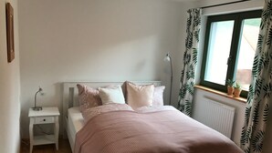 A bedroom with a bed, nightstand, lamp, window with curtains, and a radiator.