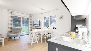 Une cuisine moderne dotée d’un évier intégré, un coin repas avec une table et des chaises, et un canapé gris.