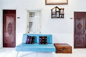 Une pièce avec un canapé bleu, deux coussins décoratifs, une commode en bois et deux portes richement décorées.