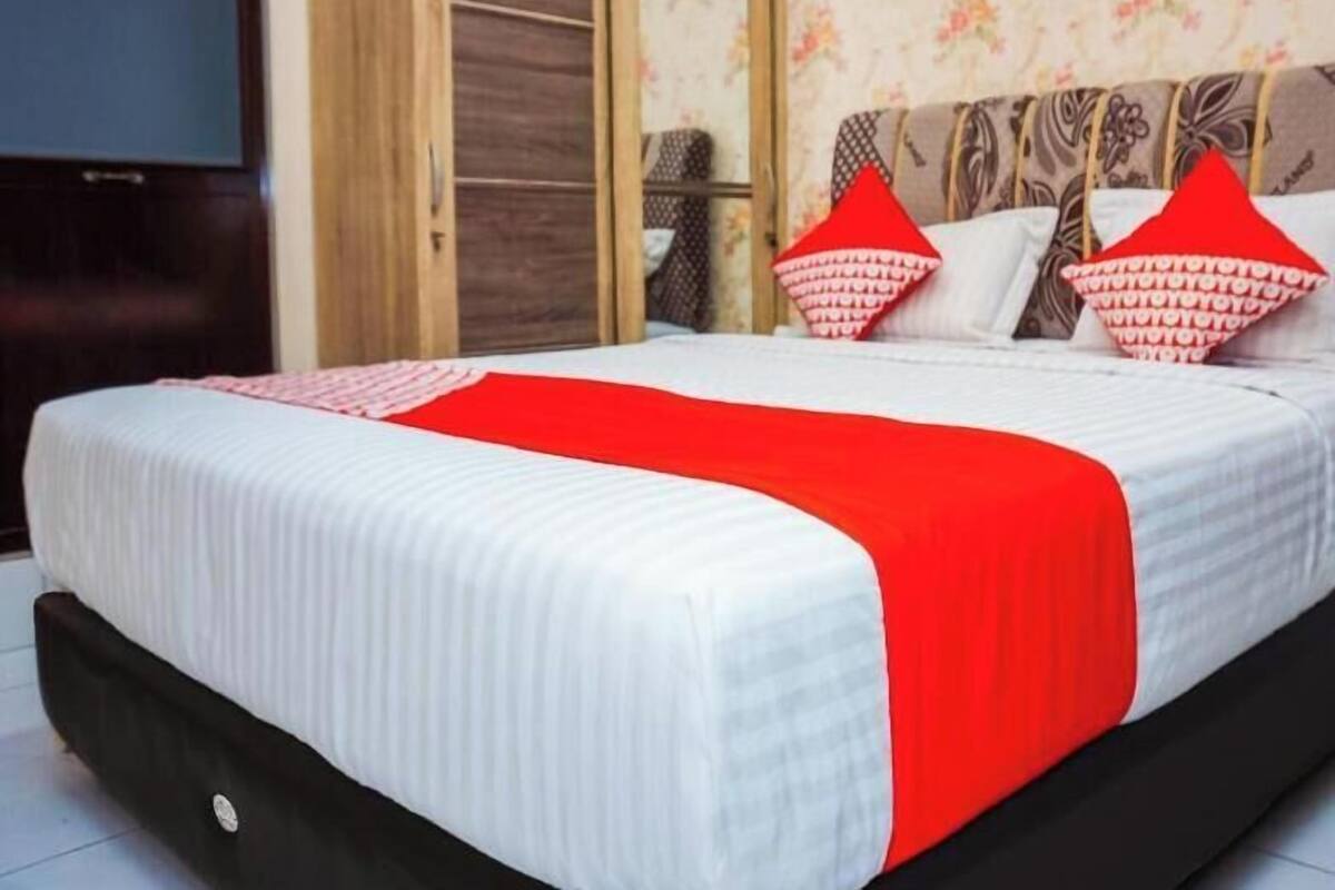 A bed with a red and white bedspread, a wooden wardrobe, and a floral wallpaper.