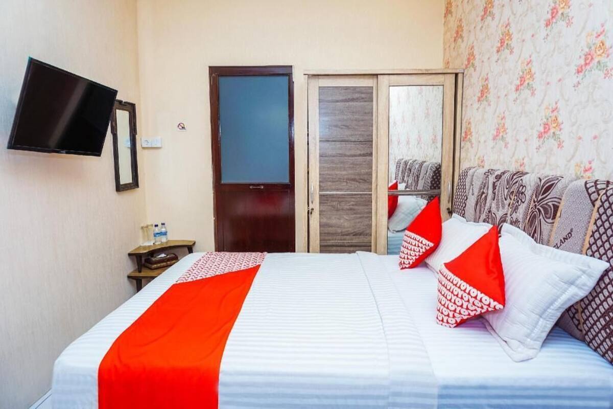 A hotel room with a bed, a TV mounted on the wall, a wardrobe, and a mirror.
