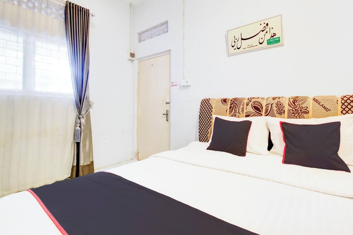 A hotel room with a bed, a window with curtains, a door, and a wall with a sign.
