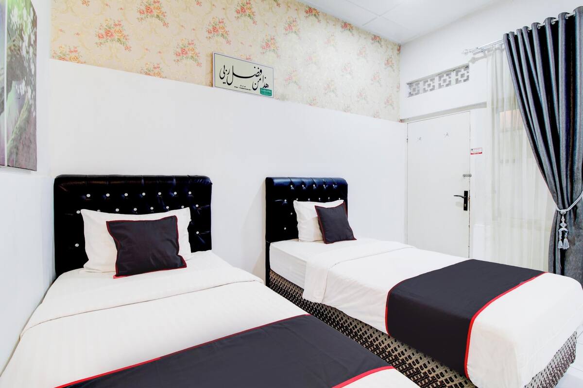 A hotel room with two beds, a floral wallpaper, a door with a sign, and a curtain.