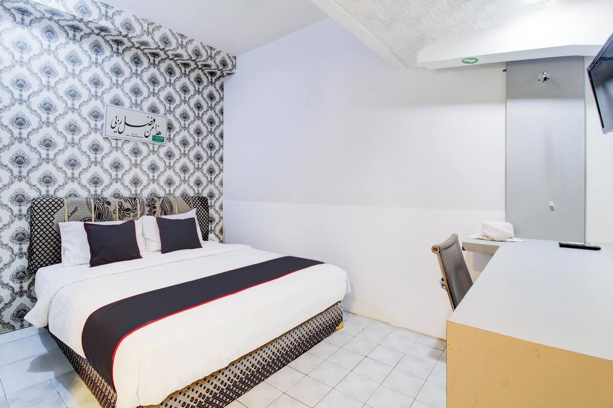 A hotel room with a bed, a bedside table, a mirror, and patterned wallpaper.