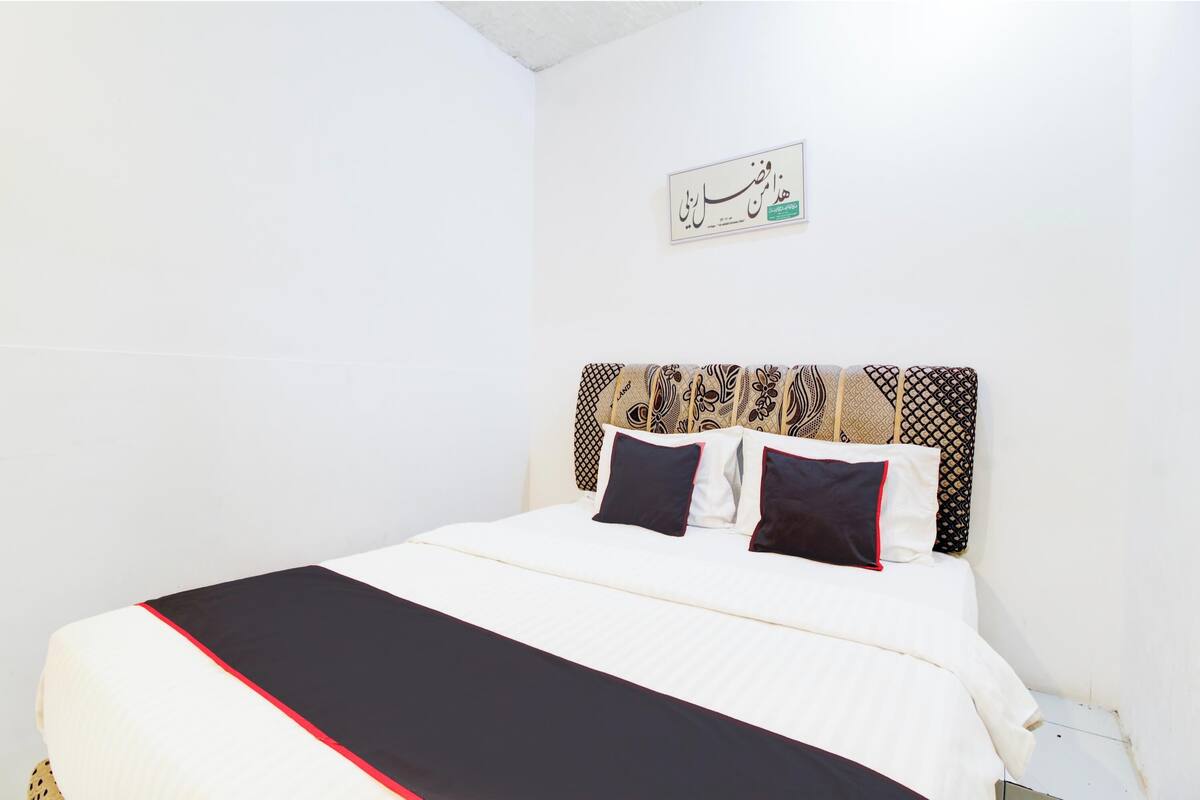 A neatly made bed with a white and black bedspread, a patterned headboard, and two black pillows.