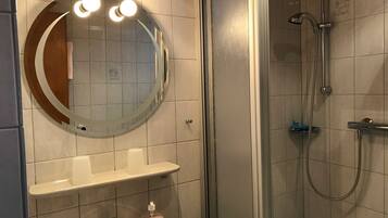 Ein Badezimmer mit rundem Spiegel, Waschbecken mit Seifenspender und Dusche mit Duschbrause.