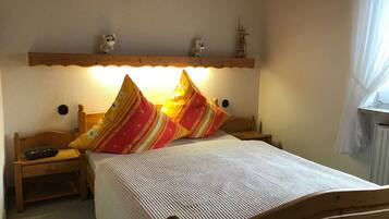 Ein Schlafzimmer mit einem hölzernen Bett, zwei Nachttischen, einem Beistelltisch, einer Wanduhr, einem Regal mit Dekoration und einem Fenster mit Vorhängen.