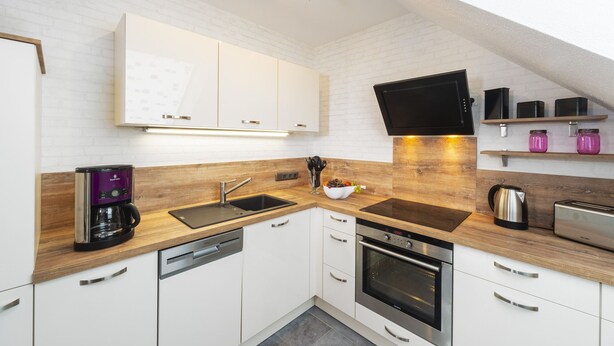 A modern kitchen with white cabinets, a built-in oven, a coffee maker, and a flat-screen TV mounted on the wall. - Apartment lifestyle quiet yet central (Steinbach-Hallenberg)