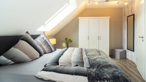 Ein Schlafzimmer mit Dachfenster, einem Bett mit gestreifter Bettwäsche, einem Kleiderschrank und einem kleinen Nachttisch mit Lampe.
