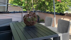 Eine Terrasse im Freien mit Tisch und Stühlen, einem Korbsessel und einem großen Sonnenschirm.