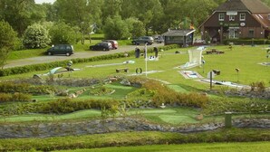Un parcours de golf doté d’un club-house, d’un étang et d’un parking où sont garées des voitures.