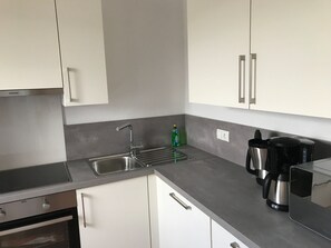 A modern kitchen with white cabinets, a stainless steel sink, a built-in oven, and a coffee maker.
