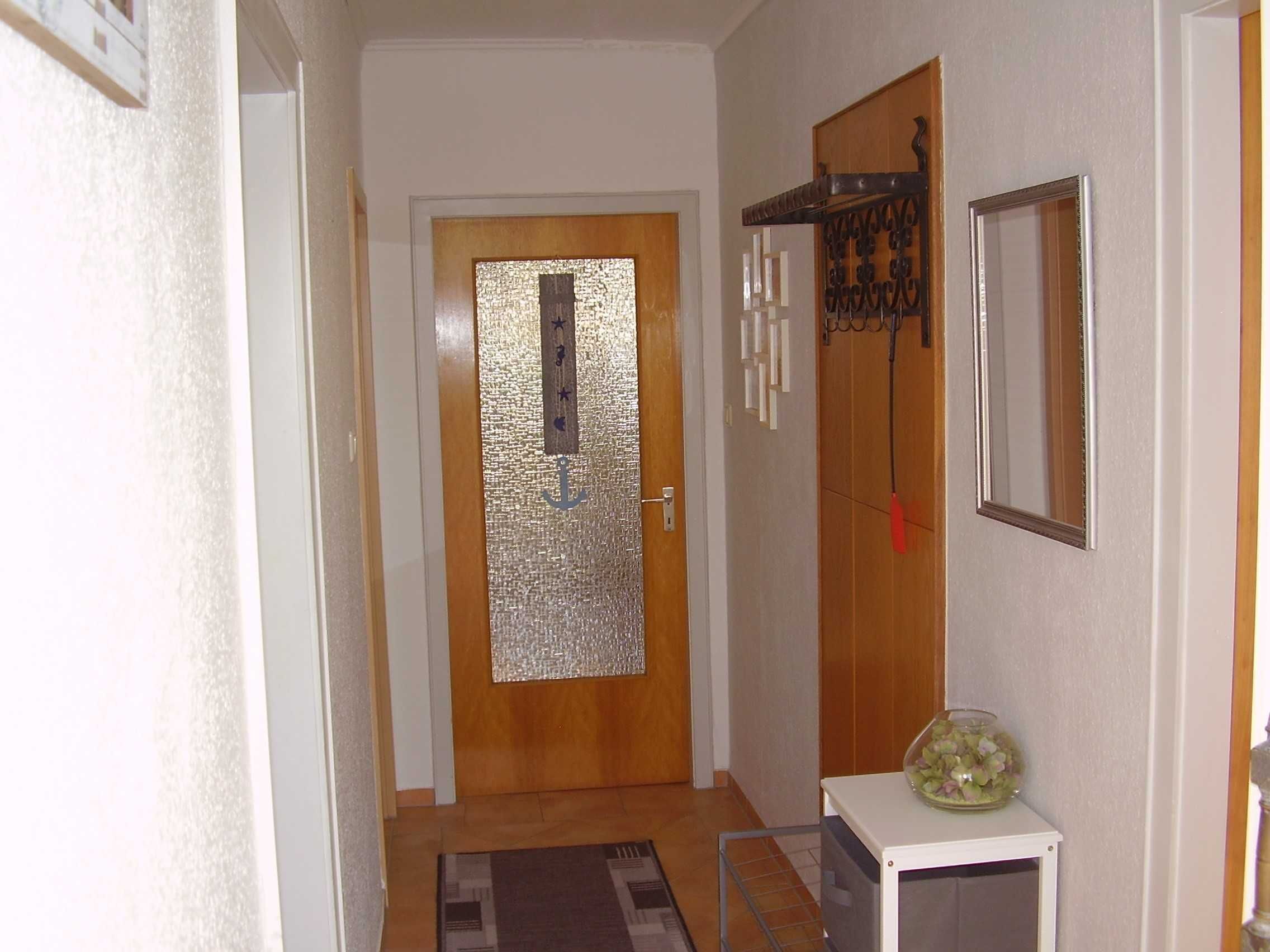 A narrow hallway with a wooden door, a small table with a glass container, and a mirror on the wall.