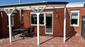 Une terrasse avec un sol en briques, une table et des chaises.