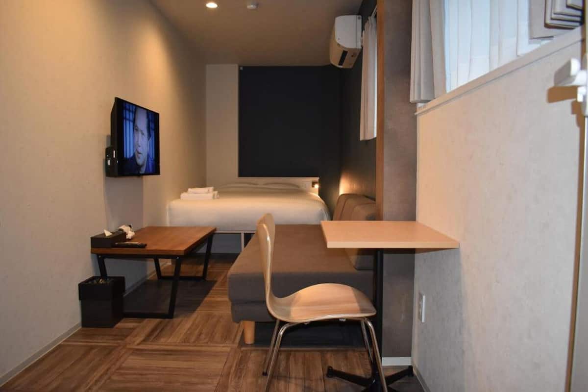 A compact hotel room with a bed, a desk, a chair, and a television.