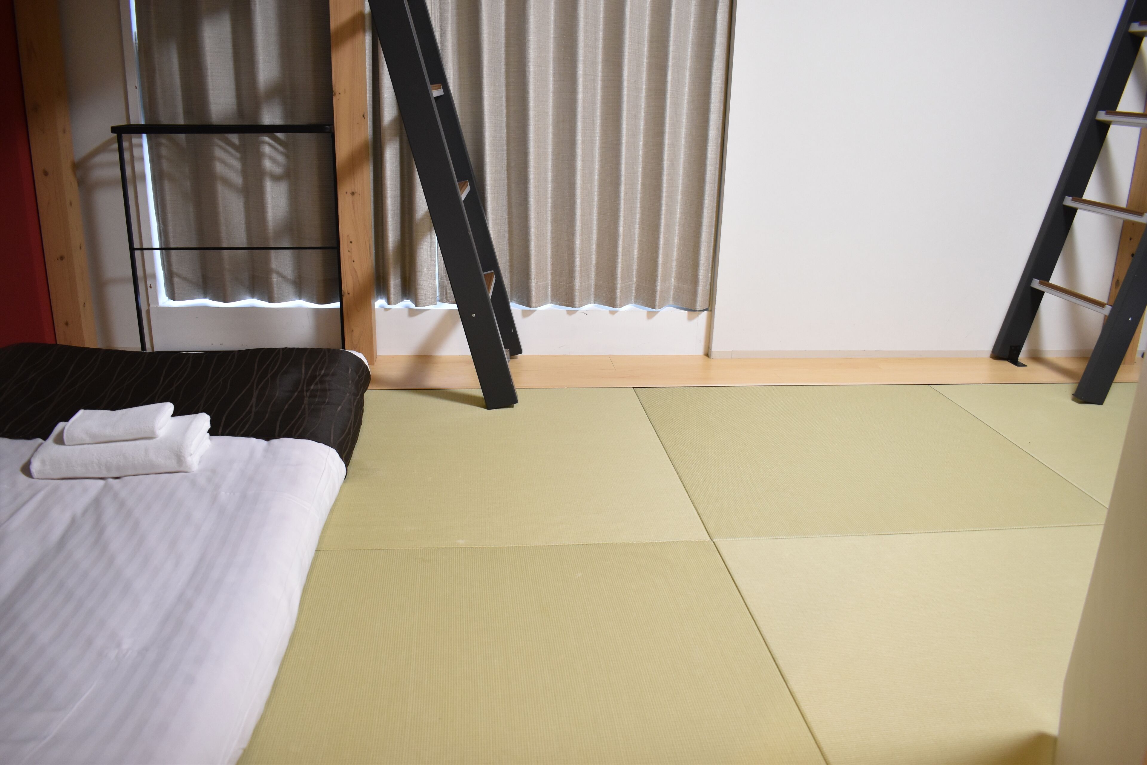 A room with a bed, a ladder, and a window with curtains.