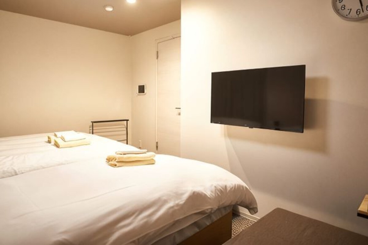 A hotel room with a bed, a flat-screen TV mounted on the wall, and a clock on the wall.