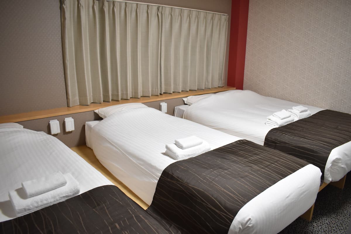 A hotel room with two single beds, a wooden headboard, a window with curtains, and a red accent wall.