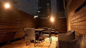 An outdoor seating area with wooden furniture and a view of tall buildings in the background. - WELLSTAY　Osaka　Shinsaibashi Apartment hotel (Osaka)