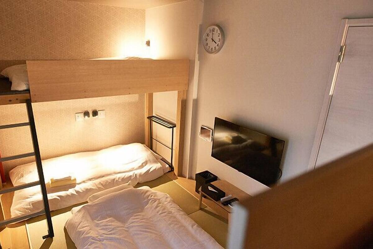 A dormitory room with bunk beds, a TV, and a clock on the wall.