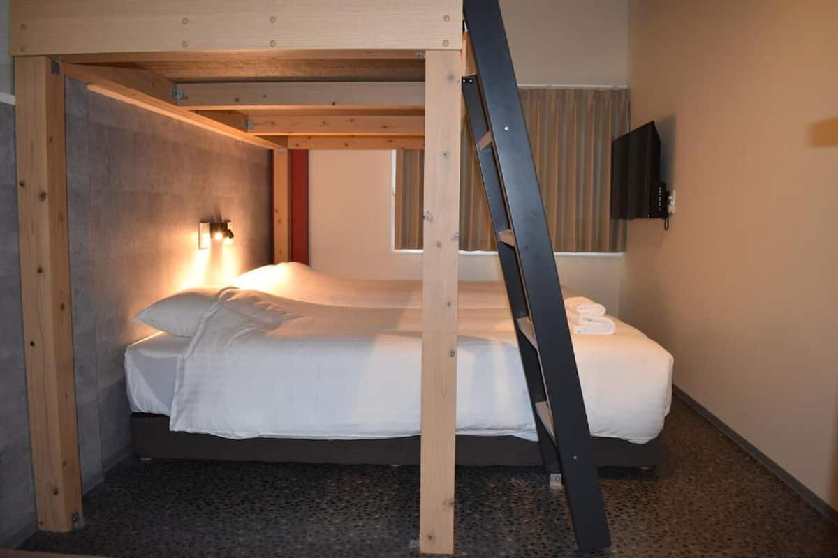 A bunk bed with a ladder, a wall-mounted TV, and a window with curtains.