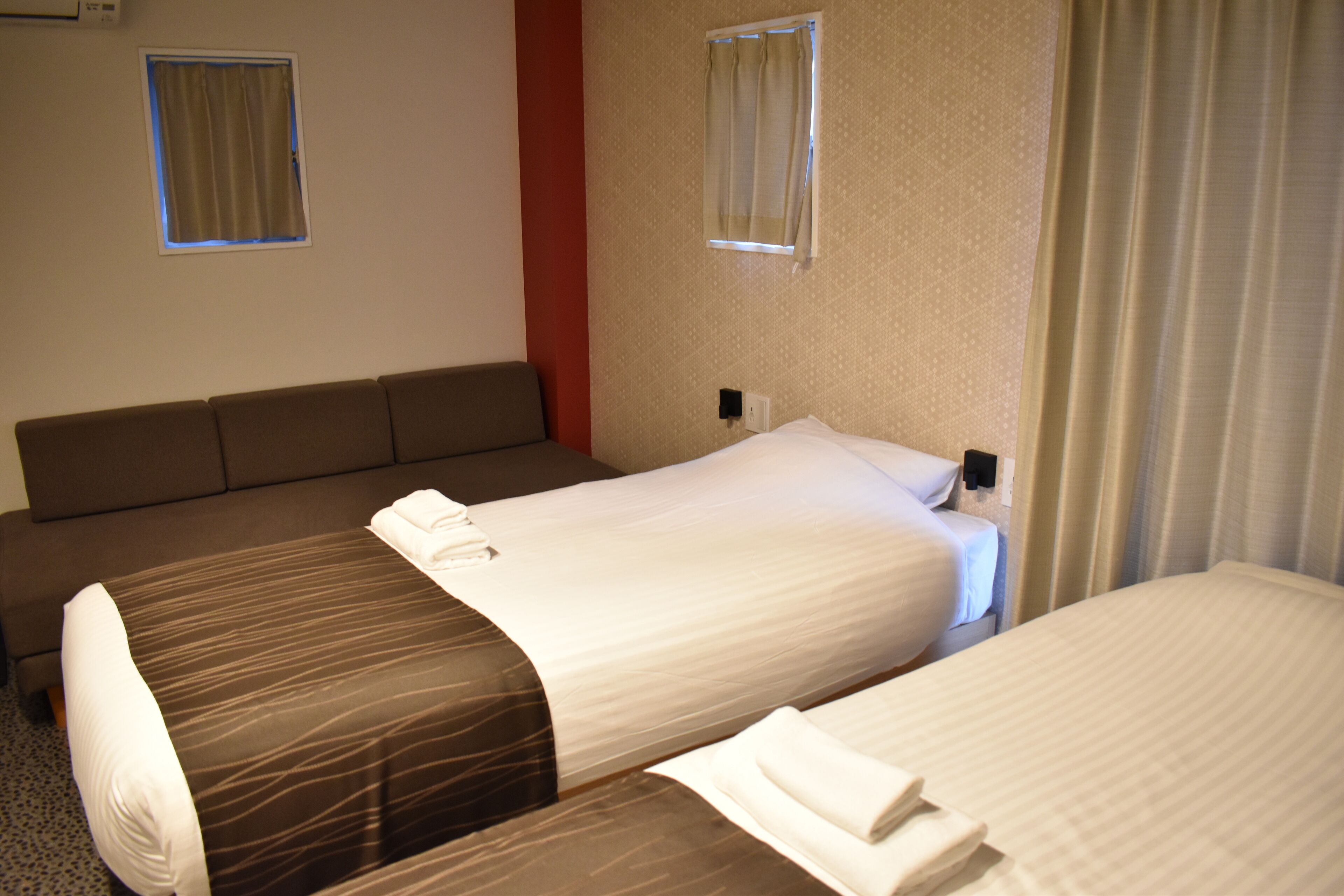 Une chambre d’hôtel avec deux lits, un canapé et une fenêtre avec des rideaux.