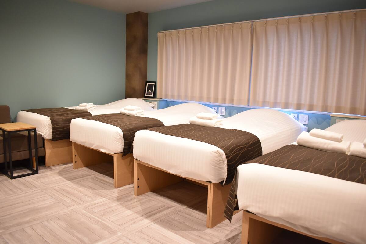 A hotel room with three single beds, a small table, and a large window with curtains.